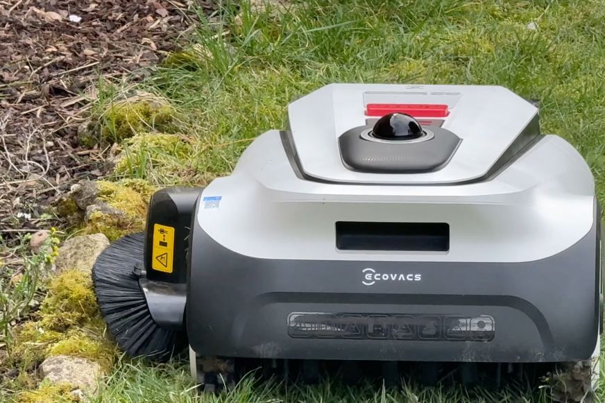 ECOVACS GOAT A1600 LiDAR PRO mit ausgefahrenem TruEdge-Trimmer an einer Rasenkante neben Pflastersteinen